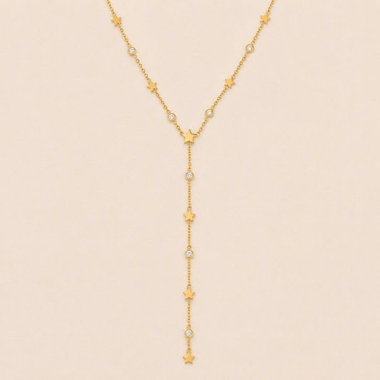 Gold Vagabonde Y NECKLACE with star and crystal stations drawn into a long lariat drop, laid flat on a beige background.