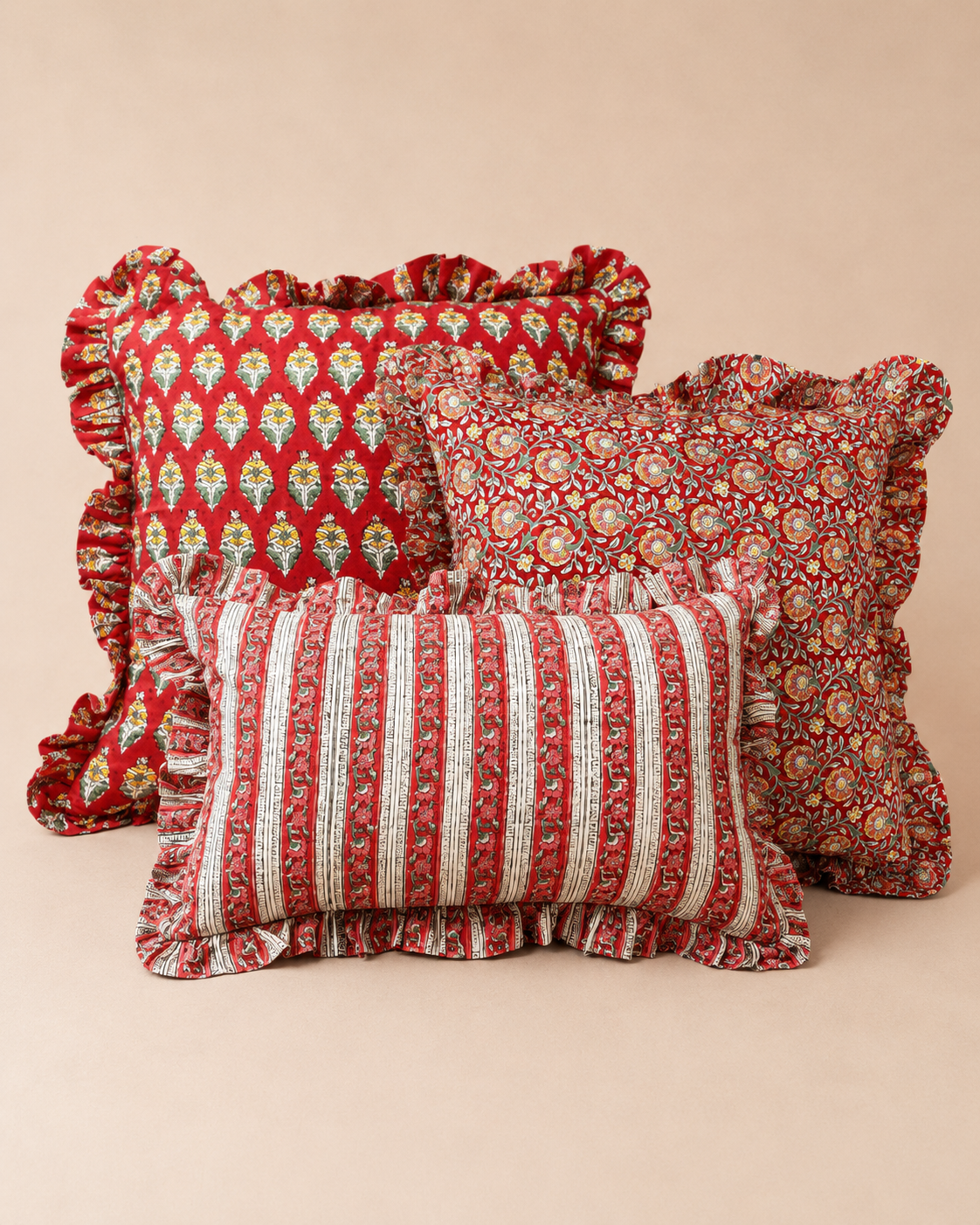 Three ruffled red cushions in leaf, floral medallion and striped patterns styled together, representing the Varsha, Suni and Sonal cushions.