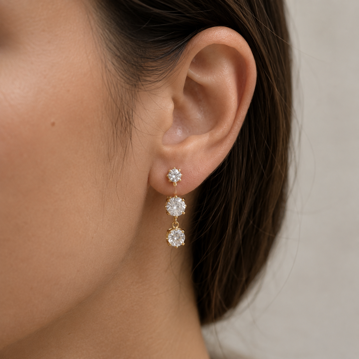 Close-up of a model wearing the gold Vega EARRINGS, a vertical line of three graduated round cubic zirconia stones.