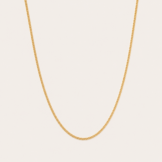 Gold curb-link chain necklace from the Vela NECKLACE design, photographed in close-up studio detail on a soft beige background.
