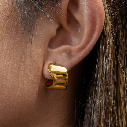Verbier Earring worn on the ear in gold, the sculptural wave hoop catching the light up close nicely.