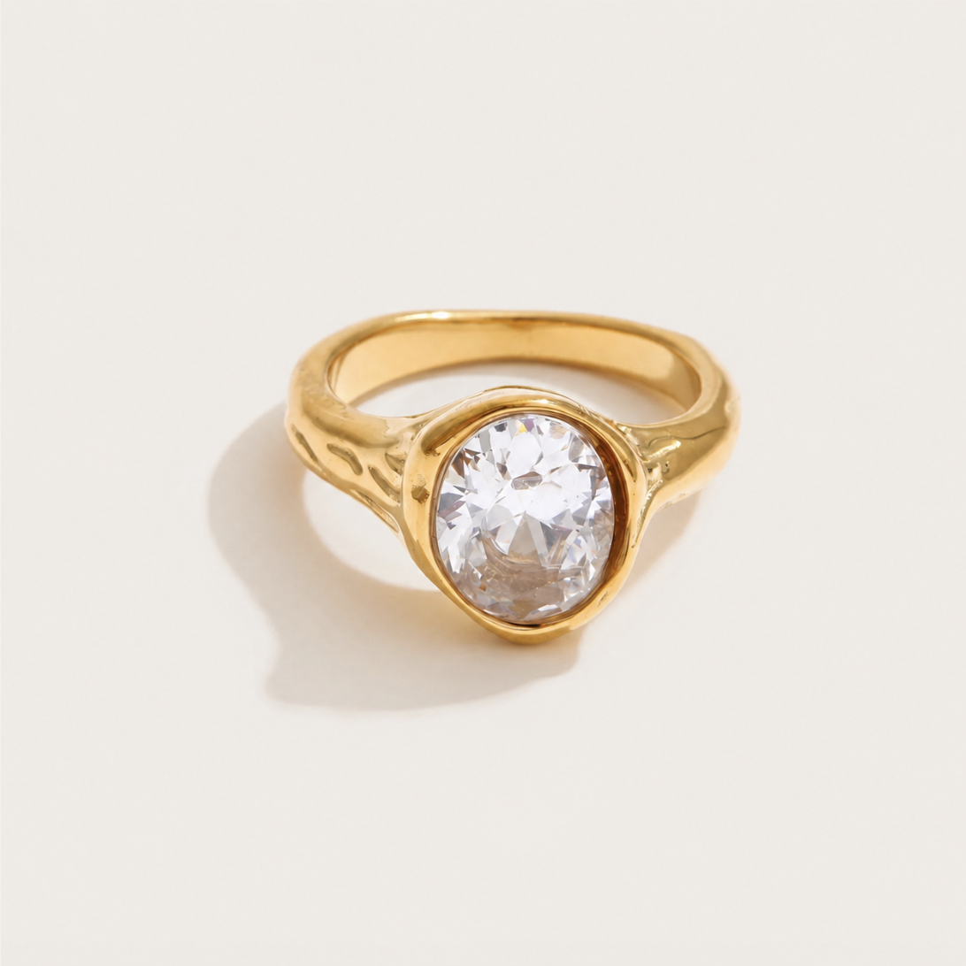 Gold bezel-set ring with a large oval white zirconia stone and a subtly textured band — Folie à Trois Vertex RING