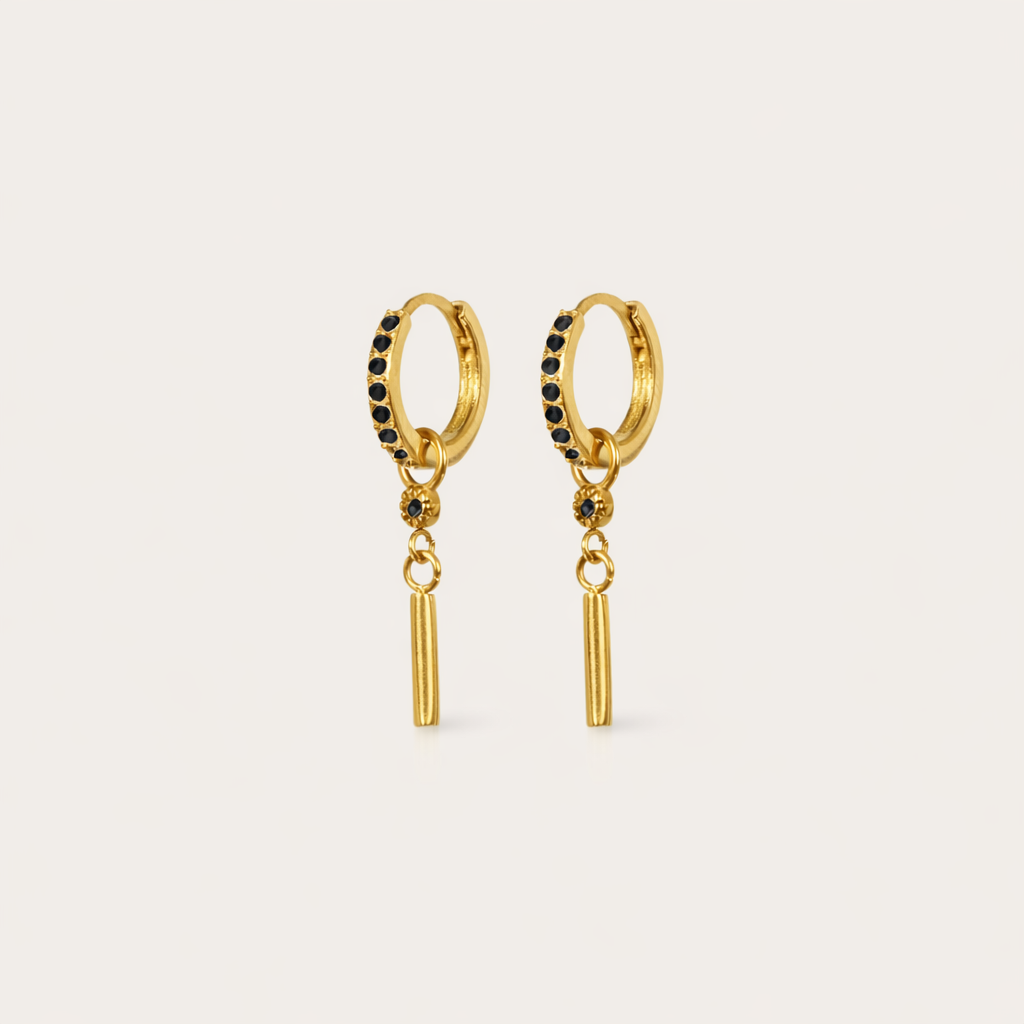 Vibrant Hues Earrings appear here in gold with black pave stones lining the hoop above a slim dangling bar charm.