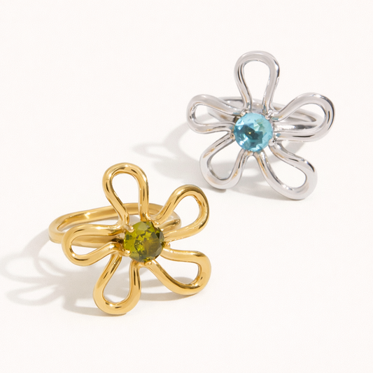 Gold and silver Vida RING styles, each a wire flower with a colored stone center, shown together on a cream backdrop.