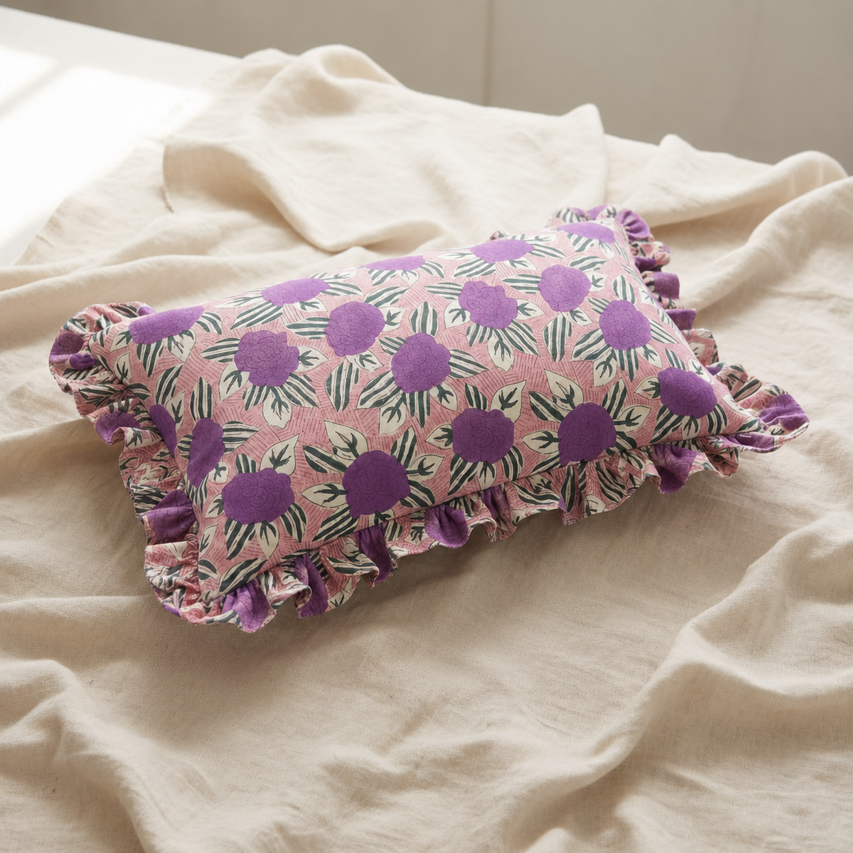 Violet Garden Rectangle cushion in its pink and purple floral print styled on a rumpled linen bed sheet in soft natural light.