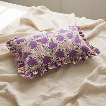 Violet Garden Rectangle cushion in its pink and purple floral print styled on a rumpled linen bed sheet in soft natural light.
