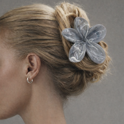 Virelle HAIR CLIP flower-shaped claw clip in grey-blue worn in an updo, with a hoop earring visible.