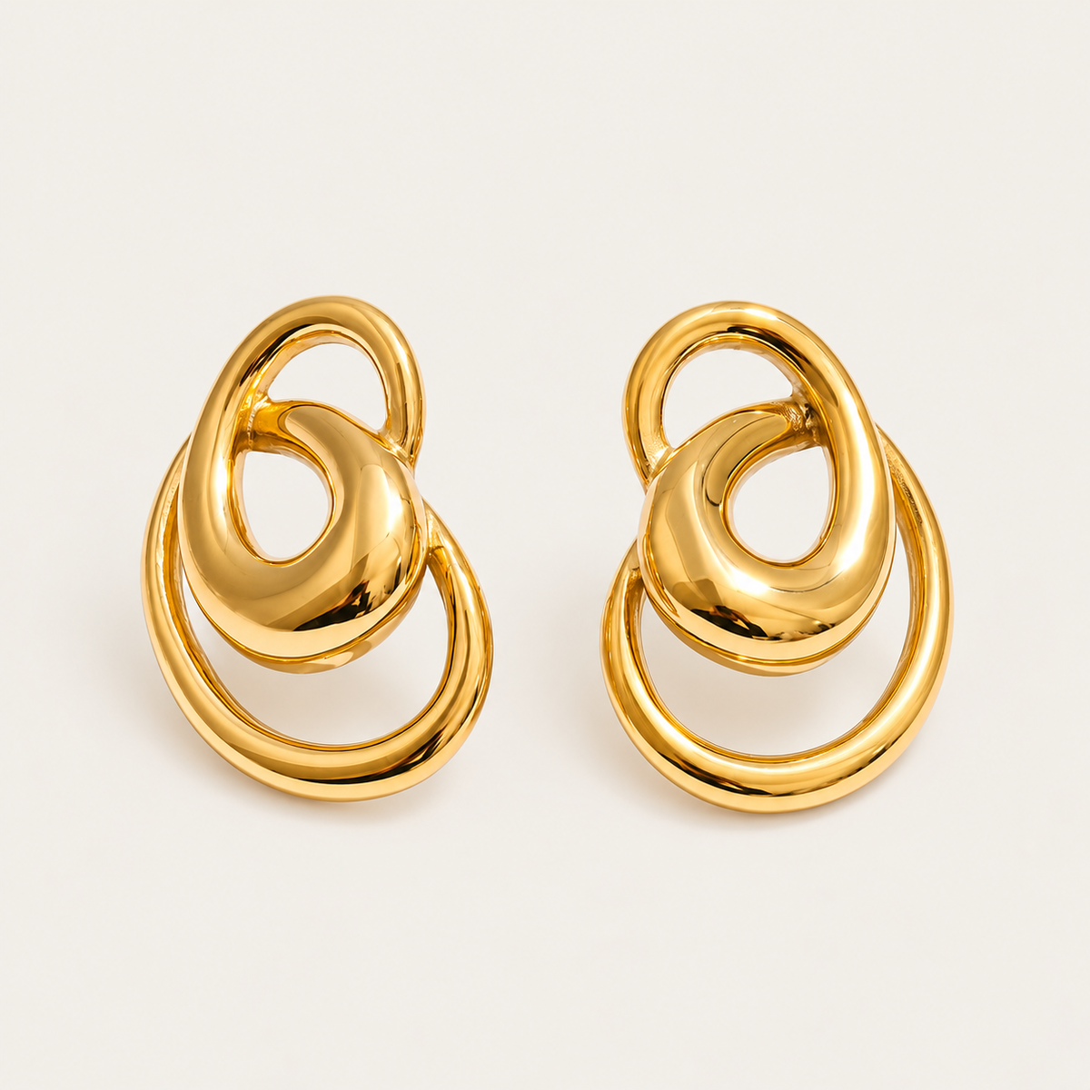 Pair of gold interlocking-ring stud earrings in a sculptural knot shape, product shot for the Folie à Trois Vortex EARRINGS.