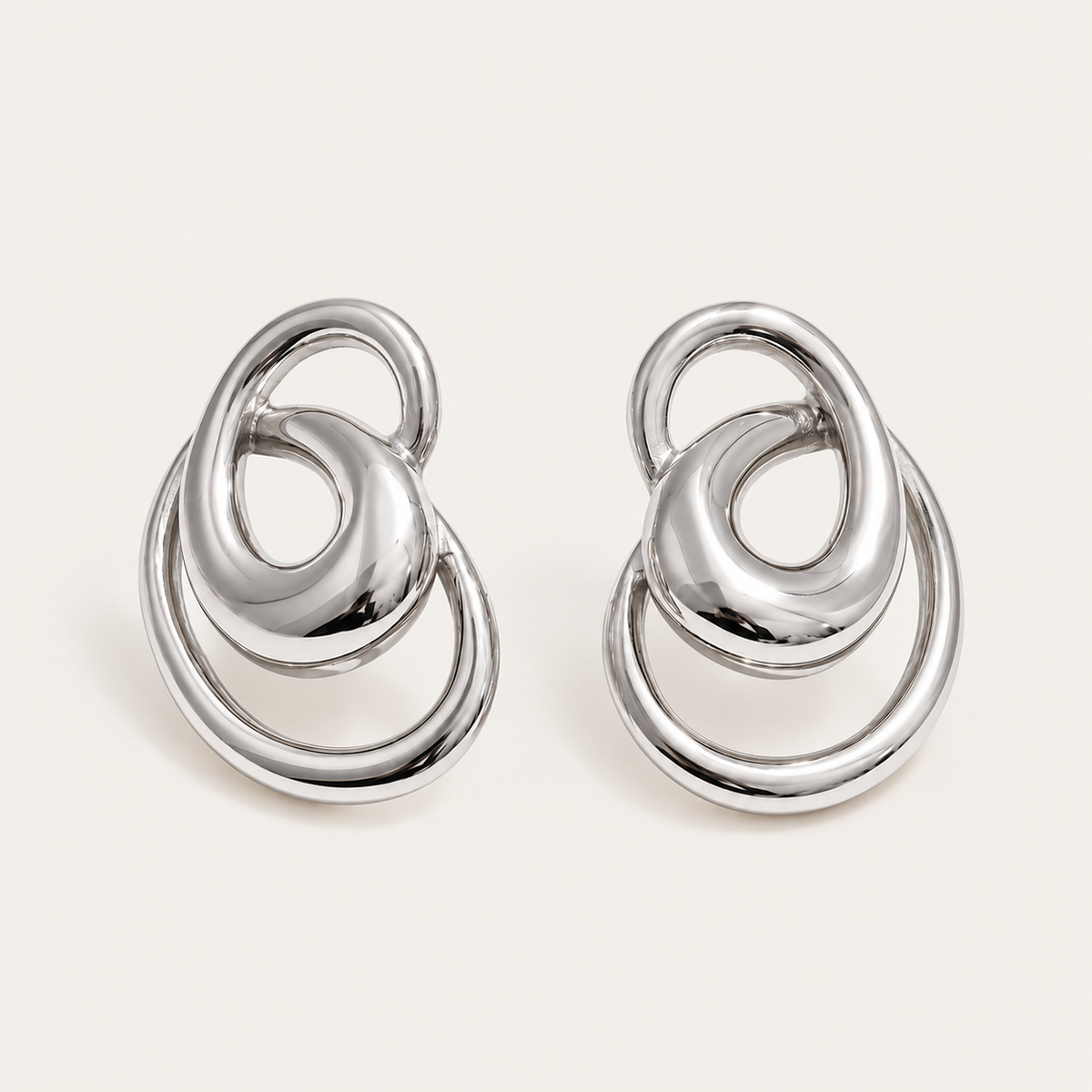 Pair of silver interlocking-ring stud earrings in a sculptural knot shape, product shot for the Folie à Trois Vortex EARRINGS.