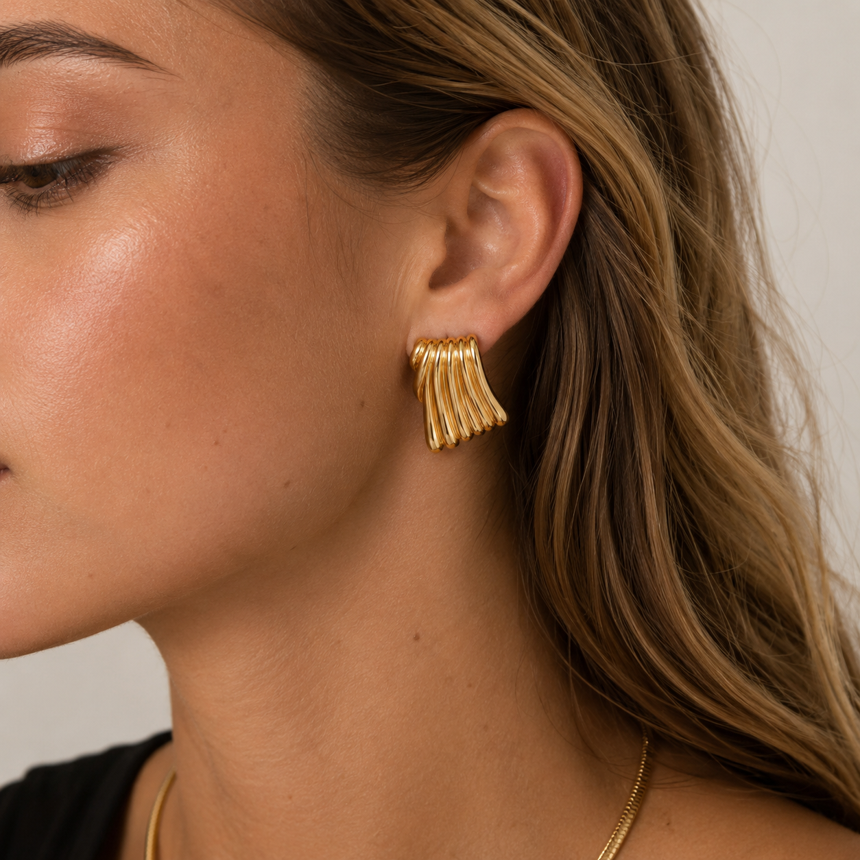 Close-up of a model wearing a fluted, fan-shaped gold Wanna be Mine EARRINGS stud on her ear, from a different angle.