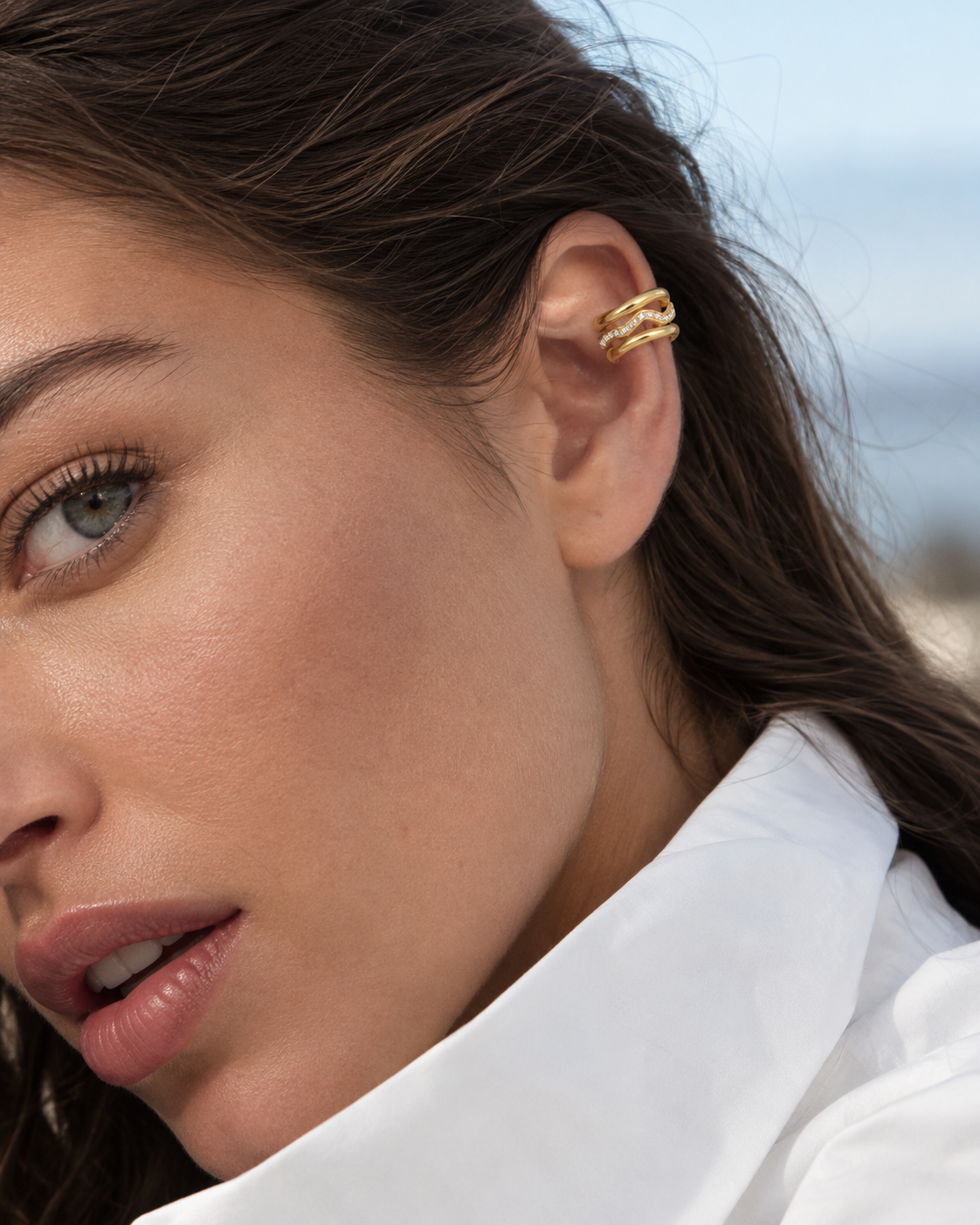 Close-up of a model by the sea wearing the gold Folie à Trois Wavelet EAR CUFF, hair swept back in the wind.