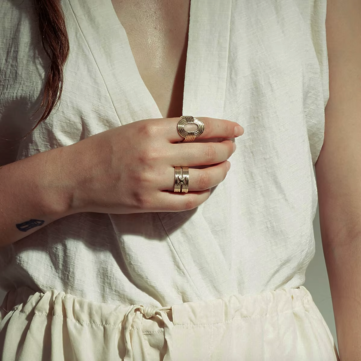 Close-up of a hand wearing the ribbed gold Whisper RING stacked with a matching textured band, resting against a linen dress.