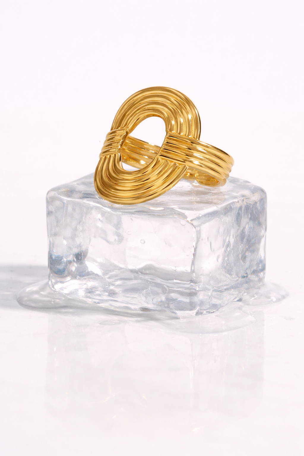 Ribbed gold Whisper RING with its interlocking oval and wrapped band displayed on a melting ice cube for a cool styled shot.