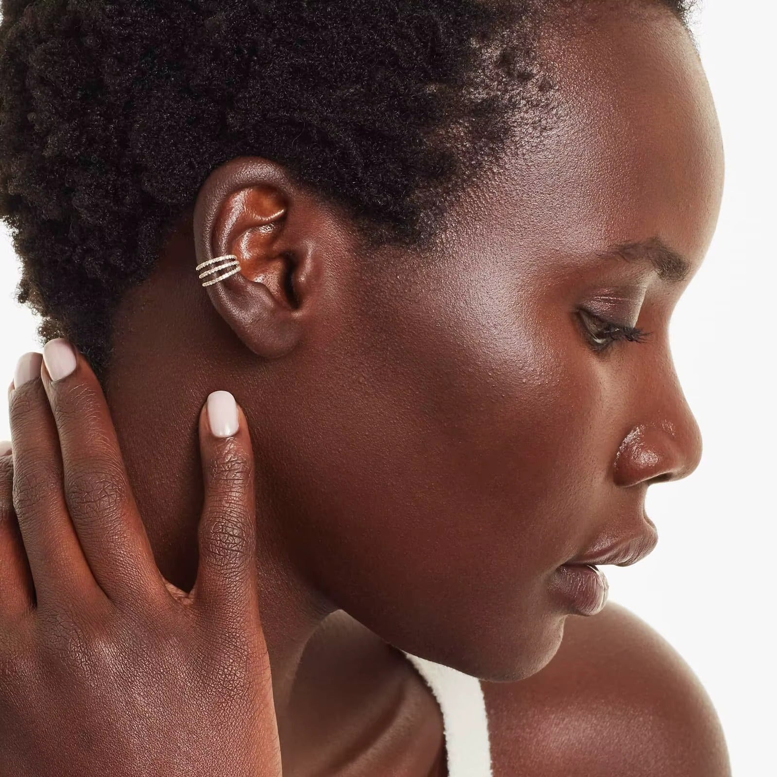 Wildcard Ear Cuff worn stacked along the cartilage of a curly-haired model, the pave crystal spiral catching light as she touches her hair.