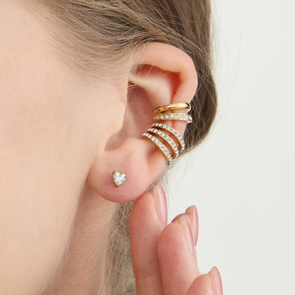 Close-up of the Wildcard Ear Cuff stacked on the cartilage above a dainty heart-shaped stud, with pave crystal rows spiraling toward the lobe.