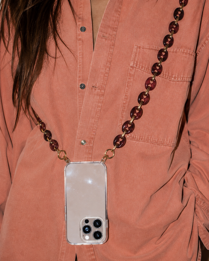Model wearing a rust-colored shirt with a phone in a clear case suspended from the Folie à Trois Wilder wholesale phone chain in wine red puffed links.