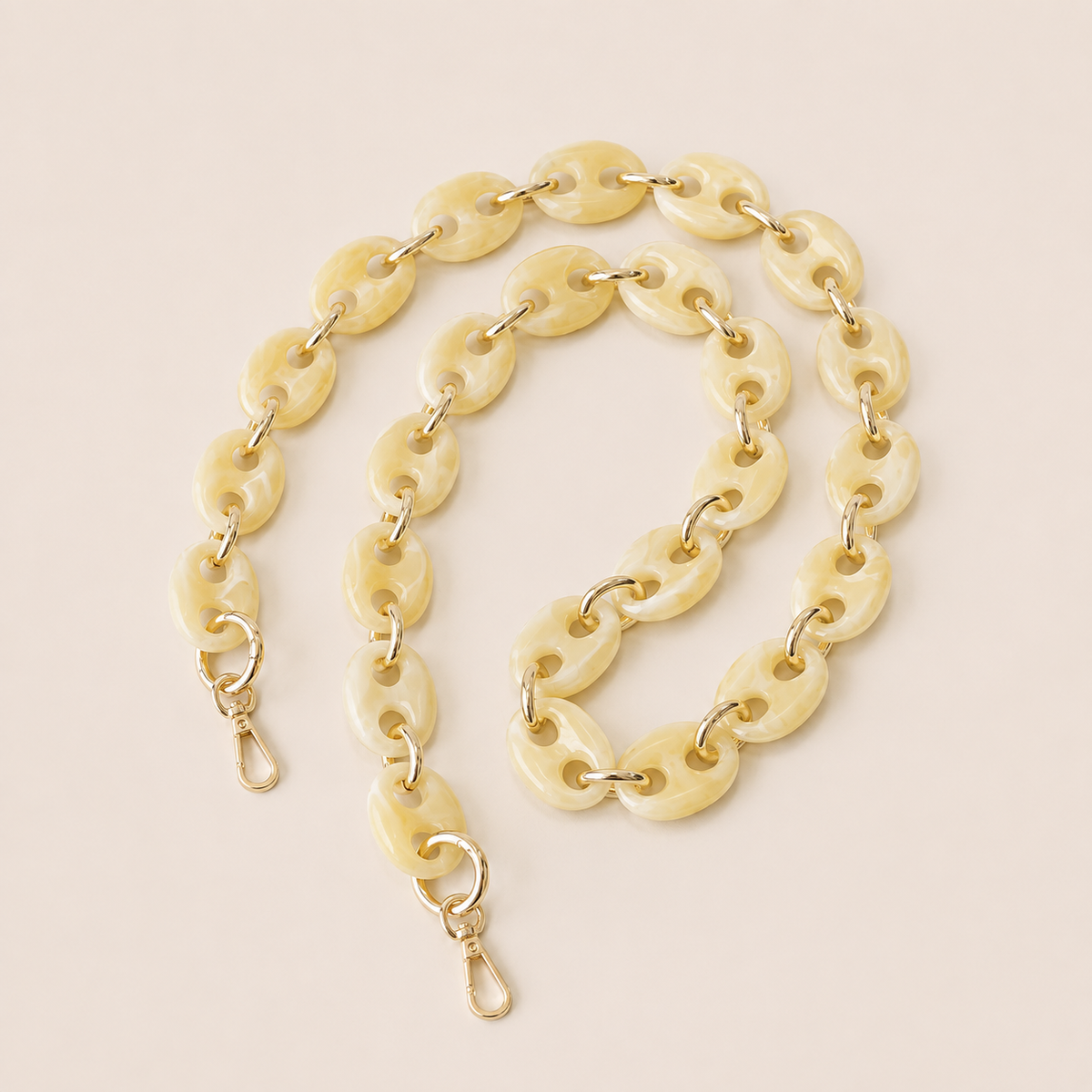 Folie à Trois Wilder long wholesale phone chain in ivory marbled puffed acetate links with gold connectors, coiled on a cream background.