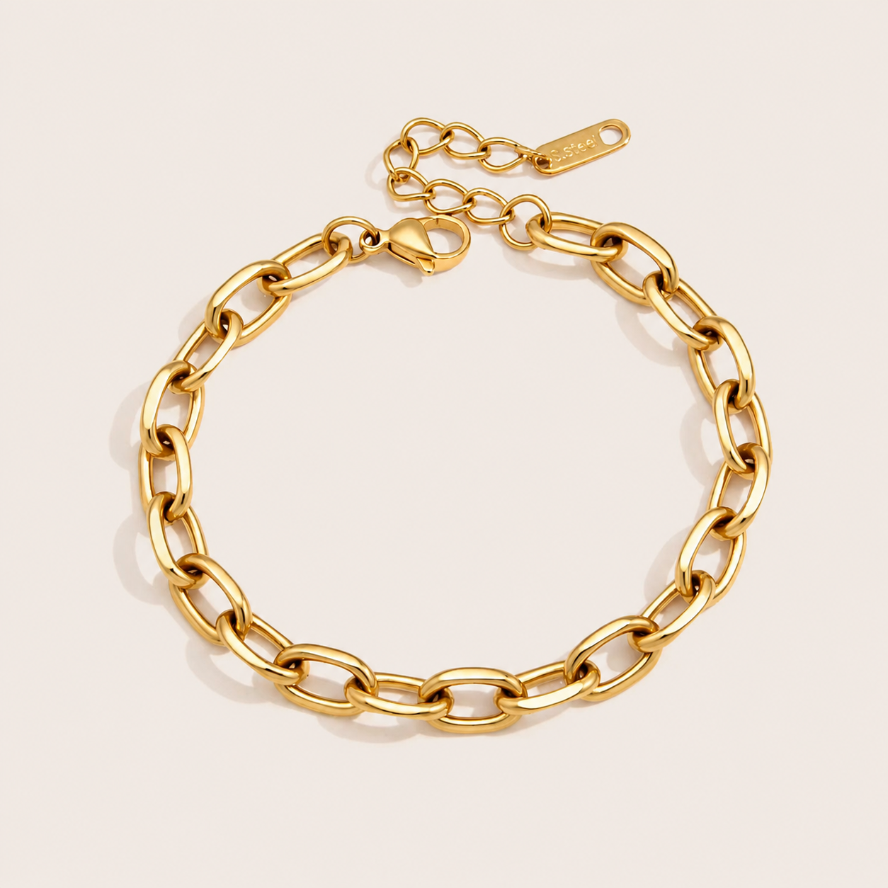 Wren BRACELET in gold with an oval cable-link chain and a small heart-shaped clasp tag, shown flat on a soft beige background.