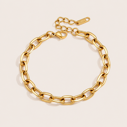Wren BRACELET in gold with an oval cable-link chain and a small heart-shaped clasp tag, shown flat on a soft beige background.