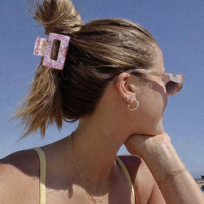 Wren HAIR CLIP worn in a low bun on blonde hair at the beach, pink and white marbled pattern, with hoop earrings visible.
