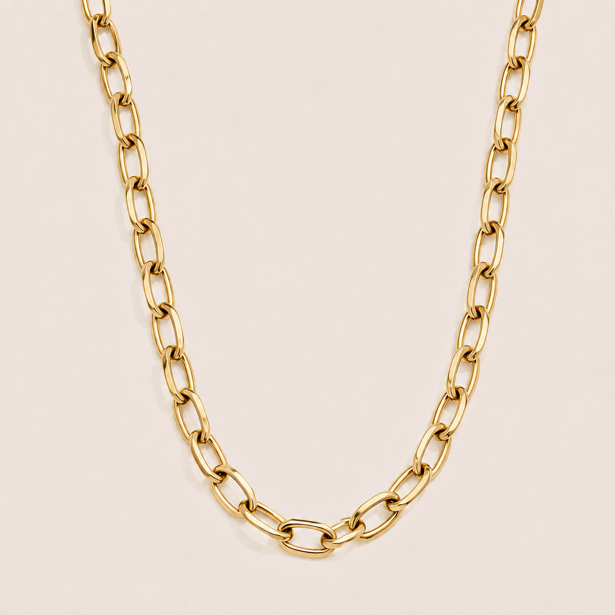Gold oval-link cable chain necklace, the Wren NECKLACE, shown in a close-up studio shot on a soft beige background.
