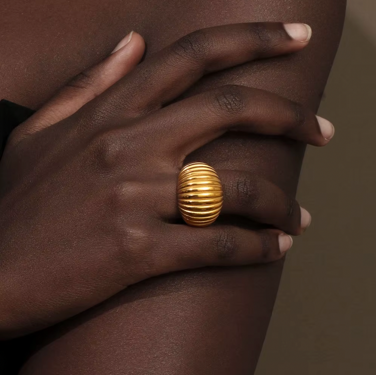 Close-up of a hand wearing the chunky gold ribbed Zelma RING, resting against bare skin.