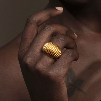 Close-up of a hand near the collarbone wearing the chunky gold ribbed Zelma RING, warm dramatic lighting.