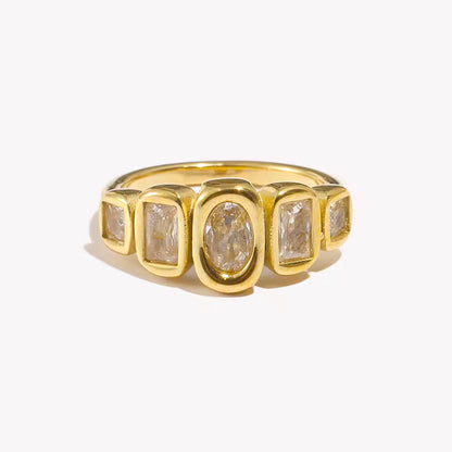 Gold ring set with five bezel-set clear stones of mixed oval and rectangular cuts in a row, shown on a cream backdrop — Zippora RING.