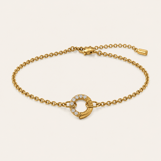 Zircon Charm BRACELET in gold with a crystal-set circle clasp connecting a delicate chain, shown flat on beige.