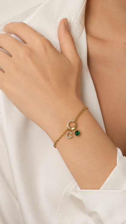 Zircon Charm BRACELET worn on the wrist, hand resting on a cream fabric, green zircon charm visible at the clasp.
