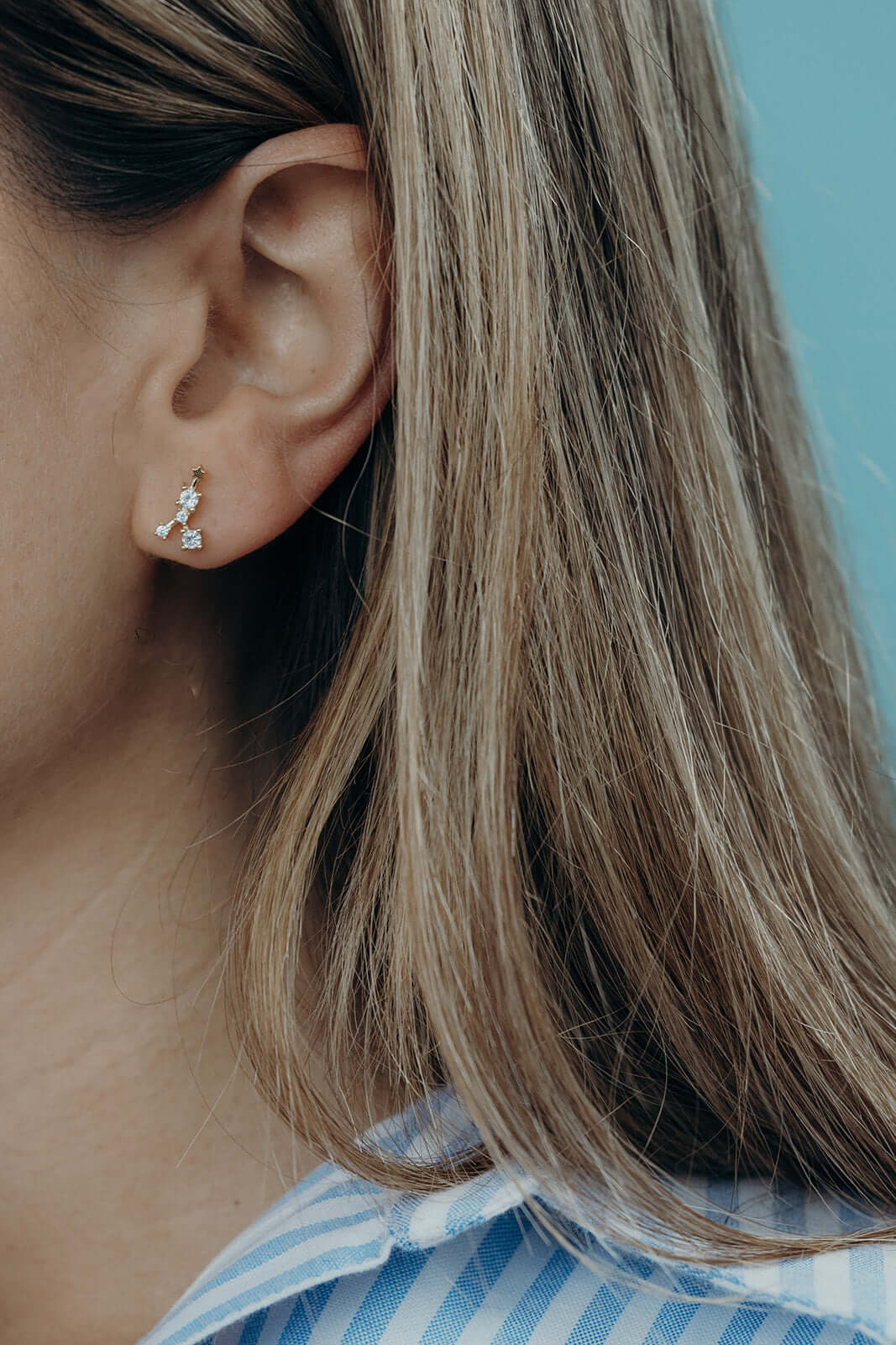 Close-up of a model's ear wearing a gold zodiac constellation stud earring set with clear crystals.
