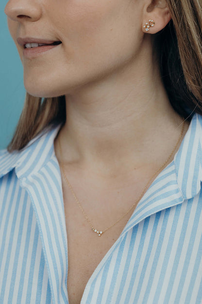 A model wears Zodiac Stud Earrings with a matching constellation necklace, both in delicate gold.