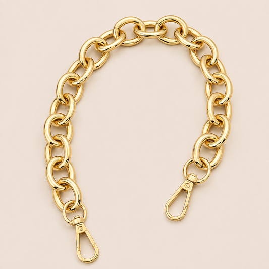 A gold-toned chunky chain link strap with two lobster clasp ends, displayed on a solid pale pink background.