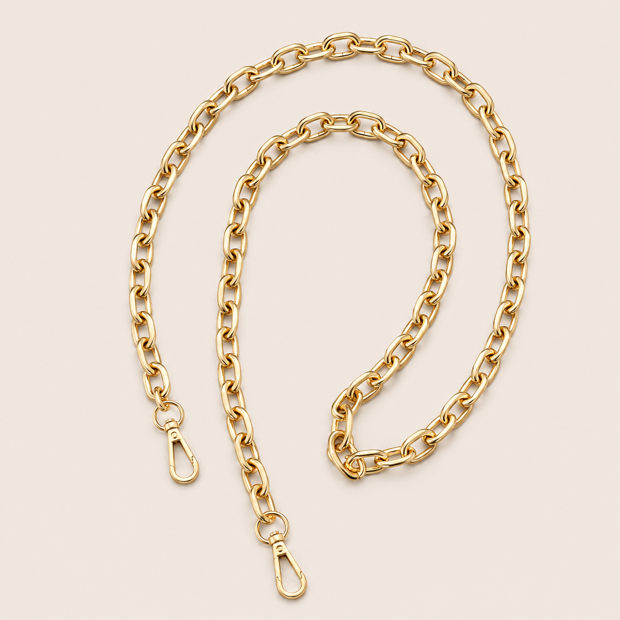 A gold-toned metal chain strap with a lobster clasp on each end, arranged in a loose loop on a light beige background.