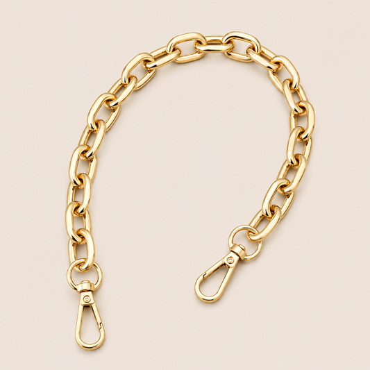A gold-toned metal link chain accessory with two lobster clasp ends, arranged in a curved shape on a light beige background.