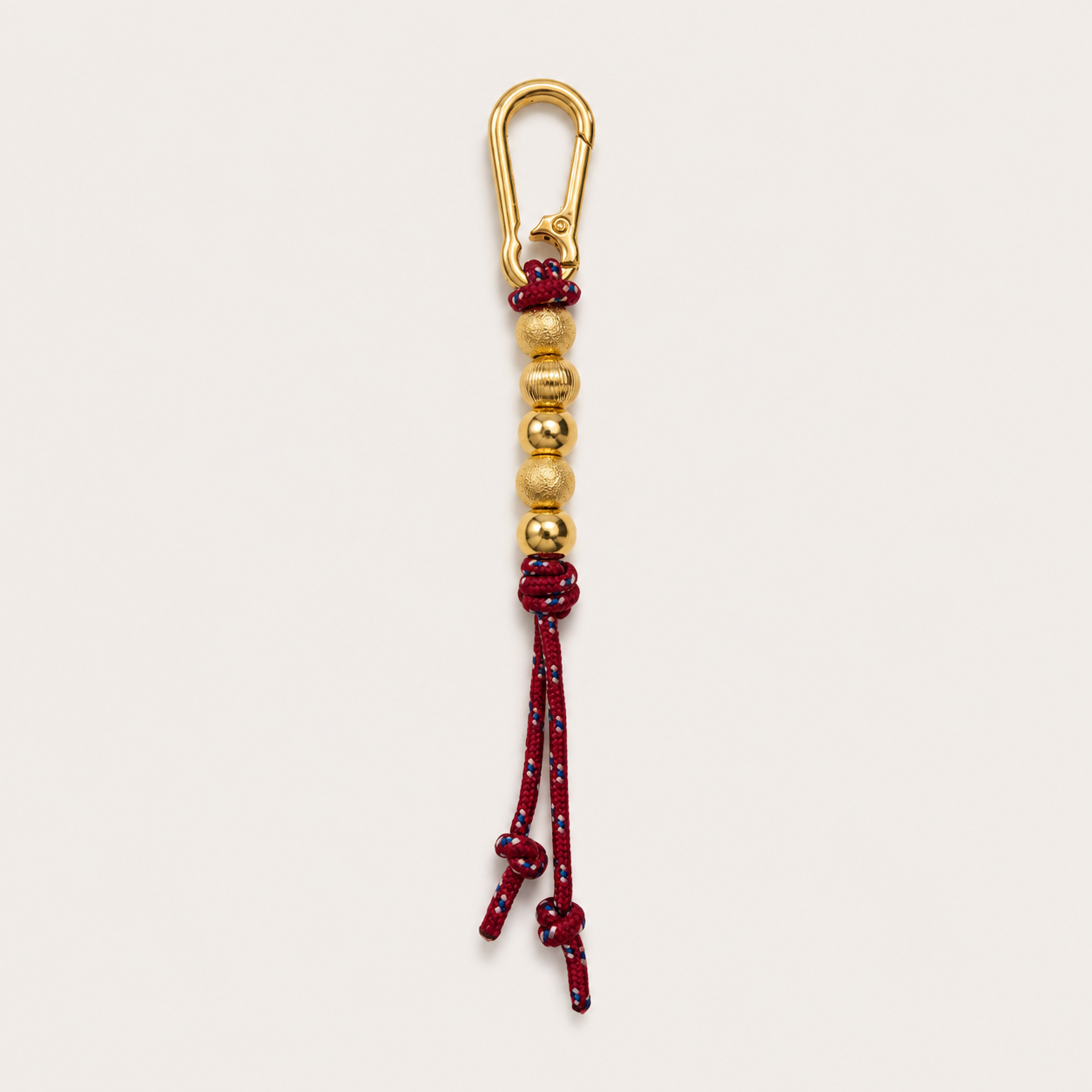 A gold-toned carabiner keychain with a red and gold beaded cord tassel, shown against a plain off-white background.