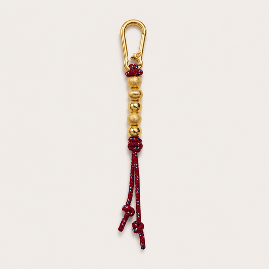 A gold-toned carabiner keychain with a red and gold beaded cord tassel, shown against a plain off-white background.