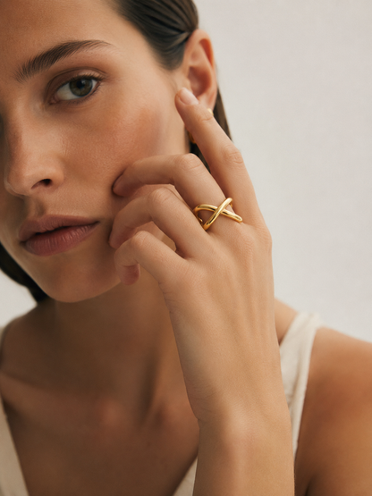 A close-up lifestyle shot of a model wearing a gold ring with an abstract, intertwined organic design on her finger.