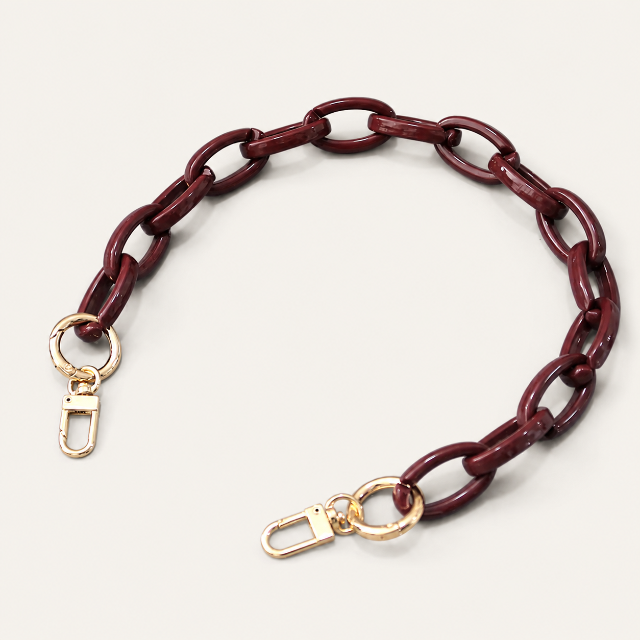 A burgundy chain link strap with gold-tone lobster clasp ends, displayed on a light beige background.