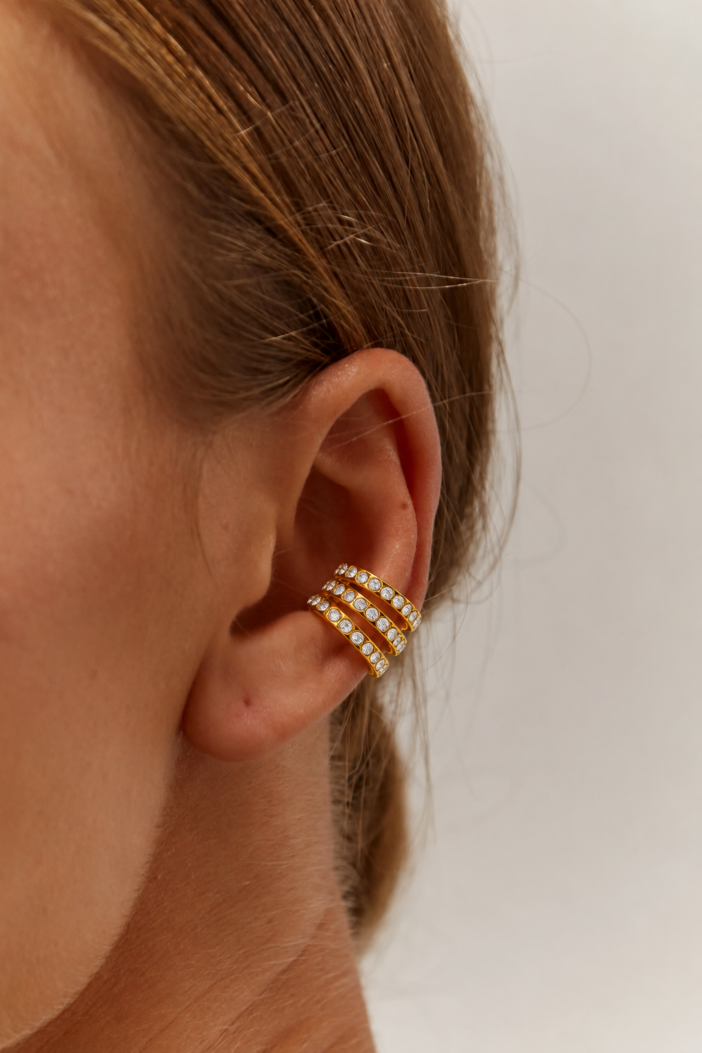 Wildcard EAR CUFF worn on the ear cartilage, three slim gold bands lined with round clear stones, close-up in profile.