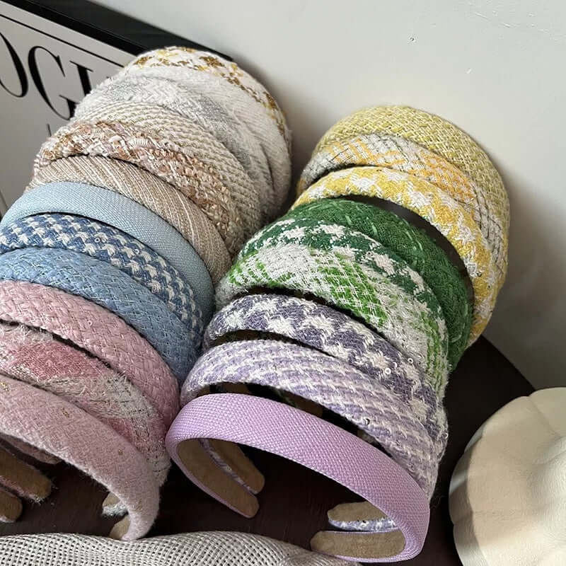 A wide assortment of tweed and boucle headbands in cream, gold, blue, green, pink and lilac stacked together as a catalog shot.