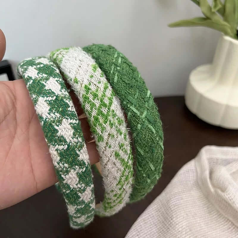 Three tweed headbands in different green patterns - houndstooth, diamond weave and solid - held together by hand.