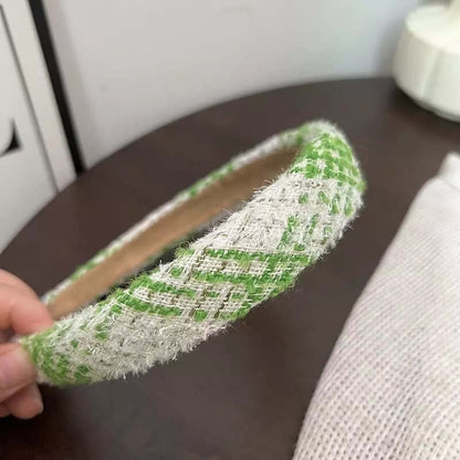 A single green and white houndstooth check tweed headband held by hand on a dark wood table.