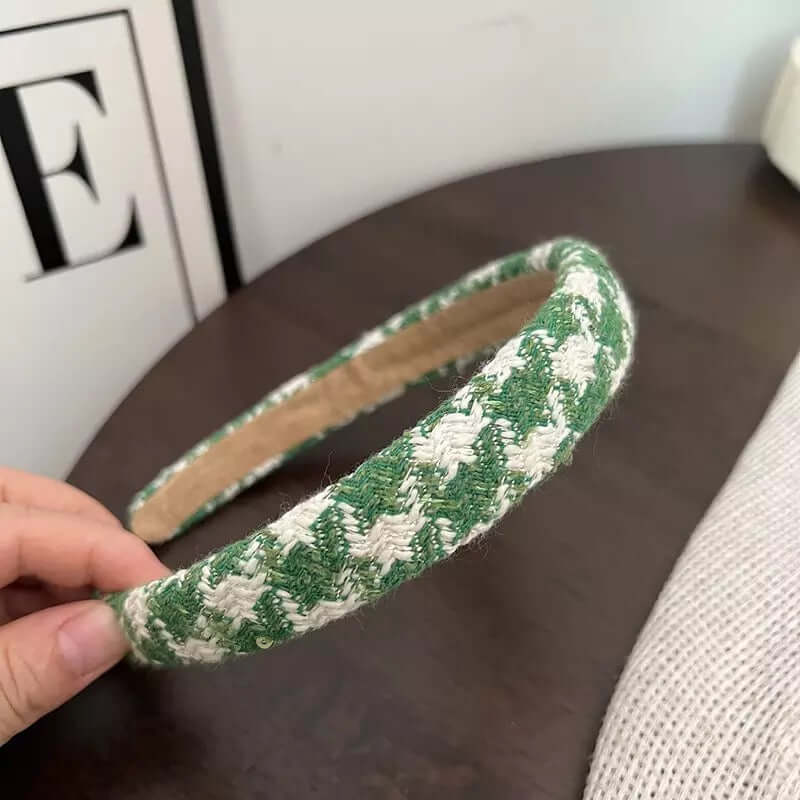 A single green and white diagonal weave tweed headband held by hand on a dark wood table.