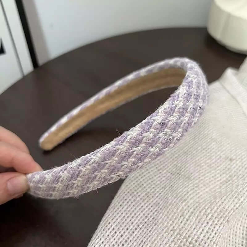 A single lilac and white woven tweed headband held by hand on a dark wood table.