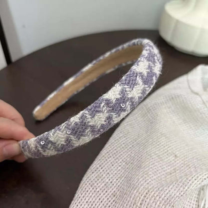 A single blue grey and white houndstooth tweed headband with small sequin detail held by hand.