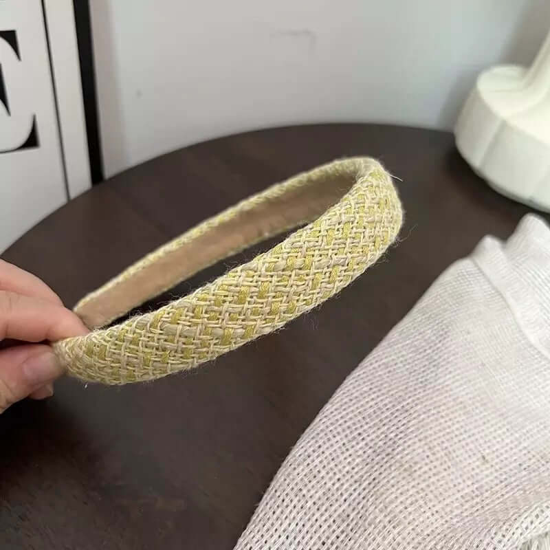 A single yellow green and cream woven tweed headband held by hand on a dark wood table.
