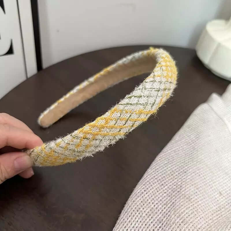 A single yellow gold and cream metallic diamond-weave headband held by hand on a dark table.