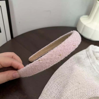 A single blush pink tweed headband with subtle gold fleck detail held by hand on a dark table.
