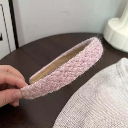 A single solid blush pink woven tweed headband held by hand on a dark wood table.